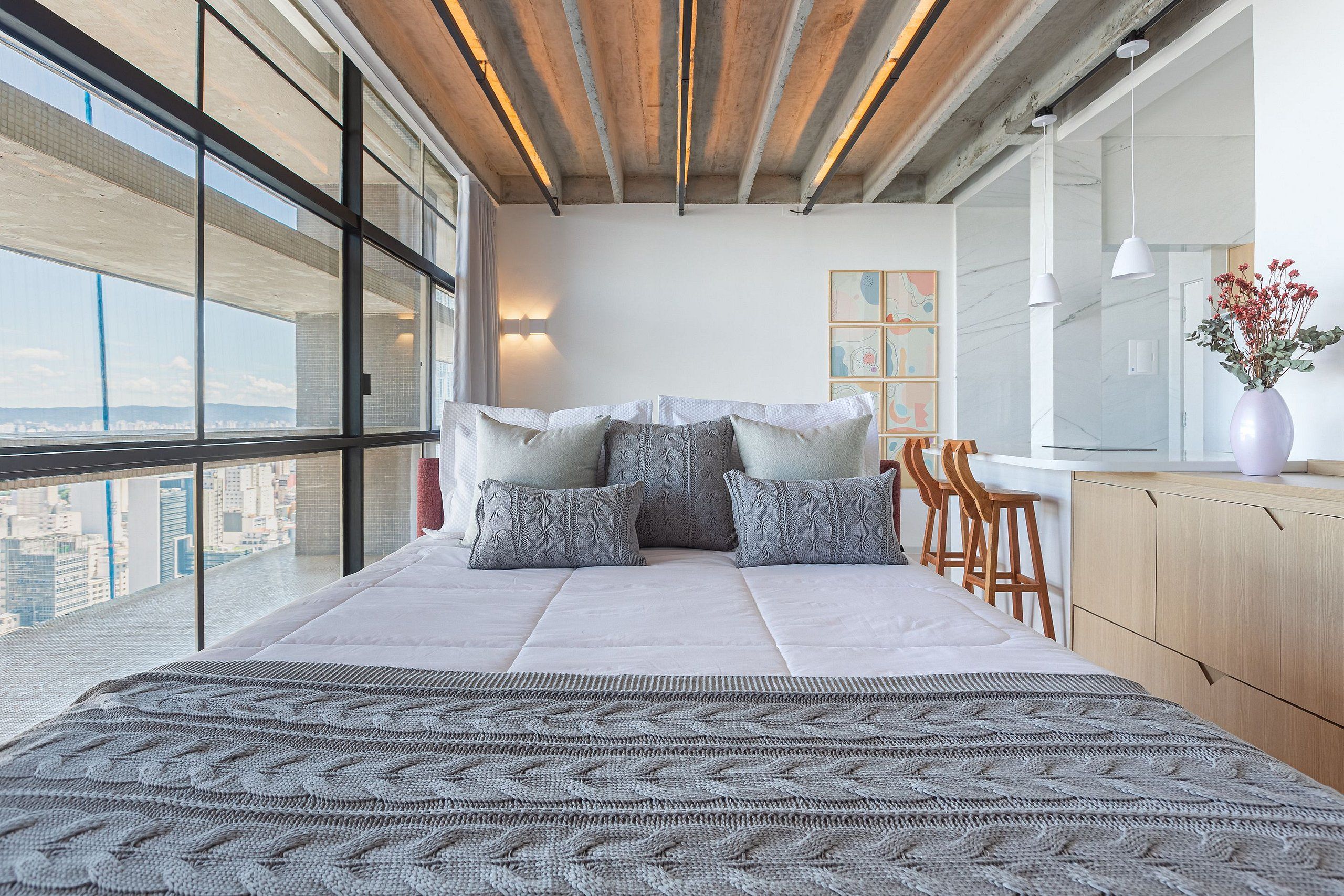 Une chambre moderne avec un grand lit, une vue sur la ville et un balcon agrémenté de chaises en bois.