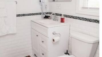 Un baño con inodoro blanco, un lavabo blanco con espejo arriba y un tapete estampado en el suelo.