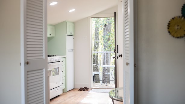 A kitchen with white cabinets, a stove, and a door leading to a balcony with a view of trees.