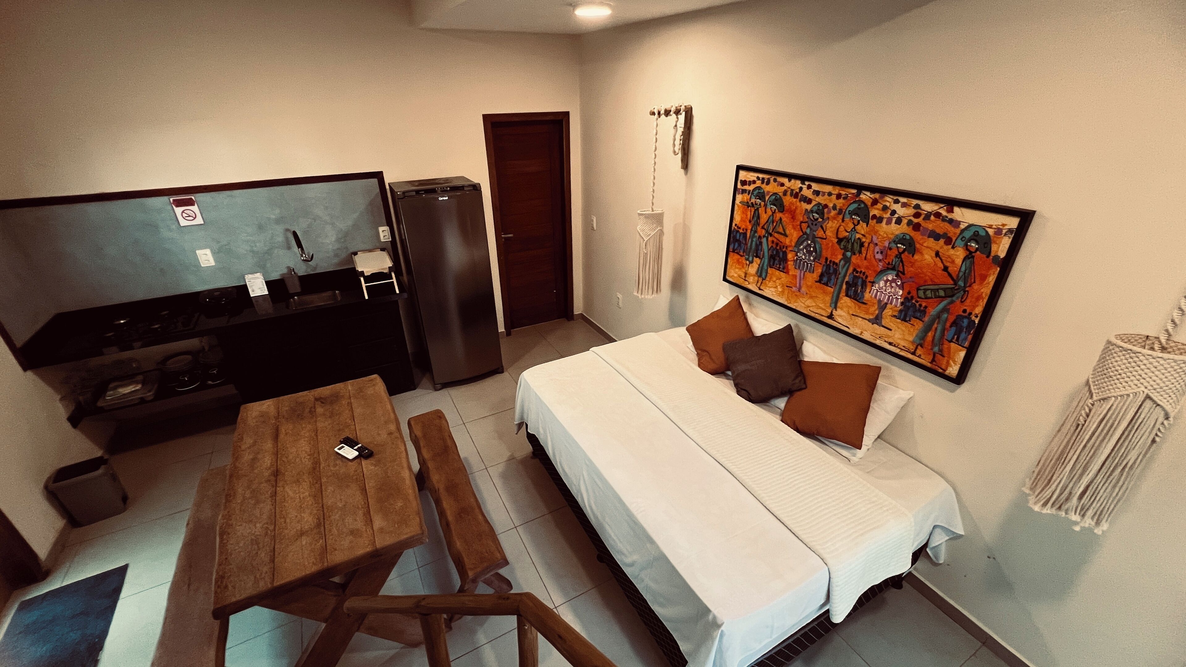 Une chambre d’hôtel de taille modeste, comprenant un lit, une télévision, un réfrigérateur, une table à manger et un tableau au mur.