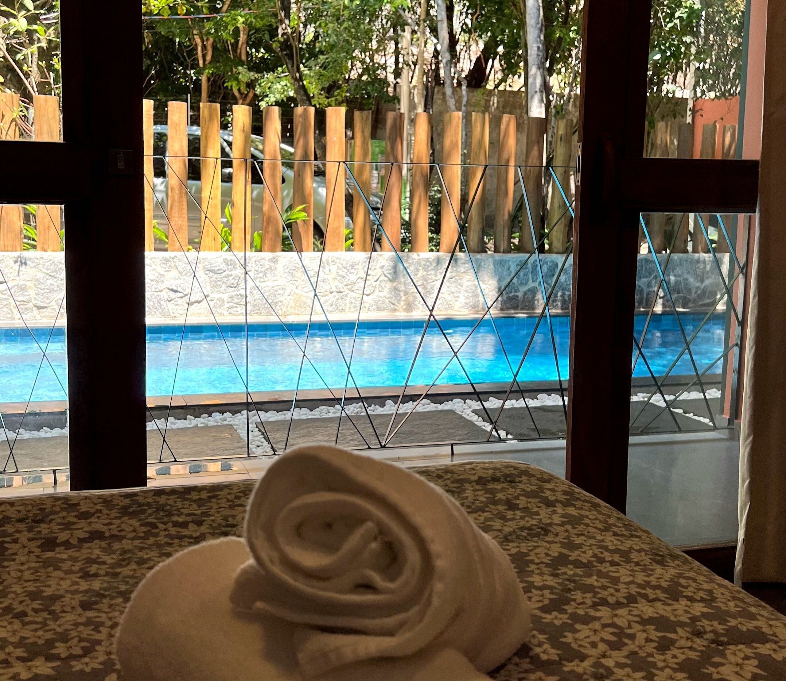 Visão de uma piscina através de uma janela, com uma cerca de madeira e uma toalha sobre uma mesa.