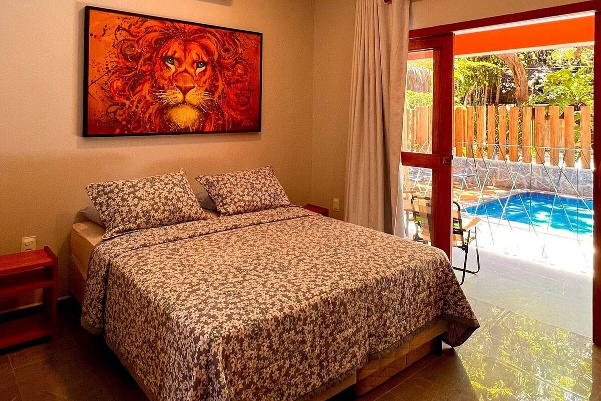A bedroom with a bed, an air conditioner, a painting, and a view of a swimming pool.