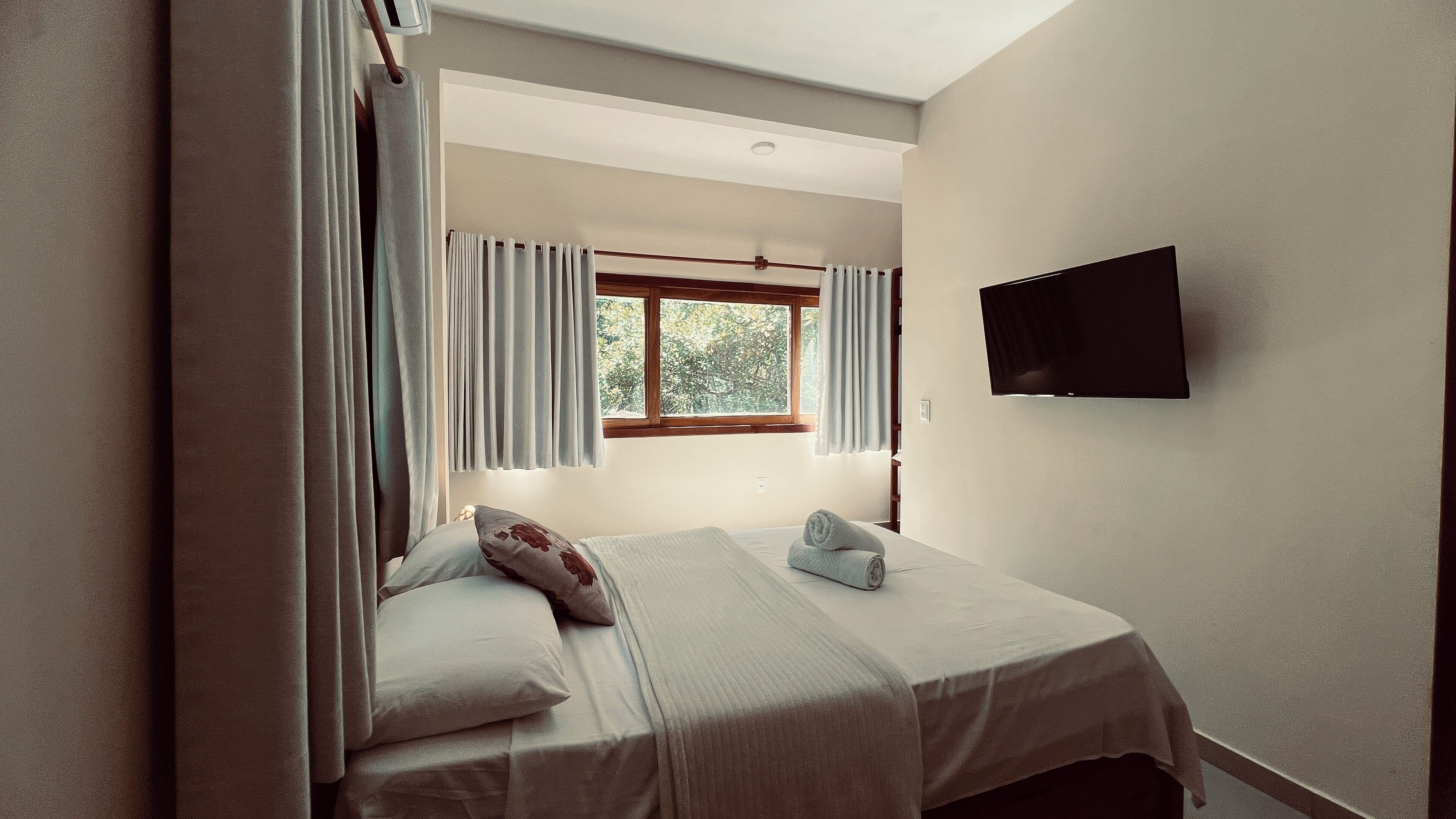 Un dormitorio con cama, cortinas, una ventana y un televisor montado en la pared.