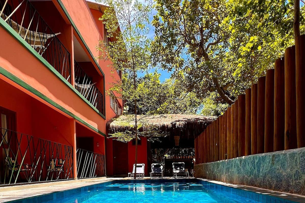 A swimming pool with clear blue water, surrounded by a red building with balconies and a wooden fence.