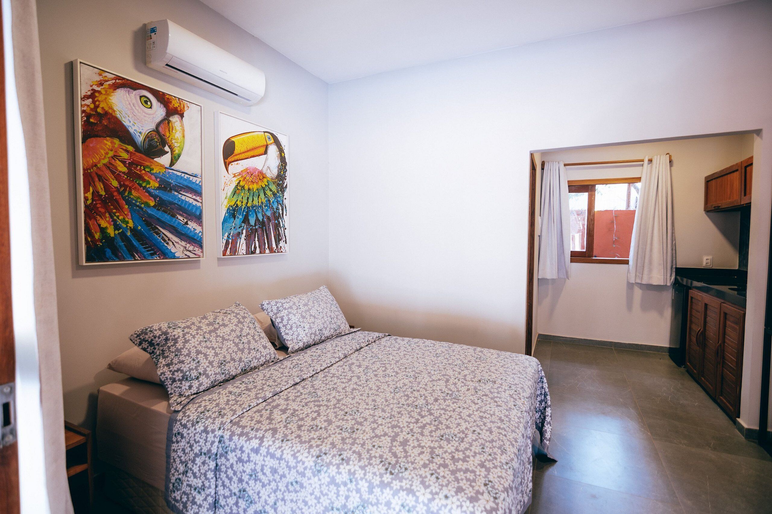 Un dormitorio con una cama, dos cuadros colgados en la pared de loros, un armario de madera y una ventana con cortinas.