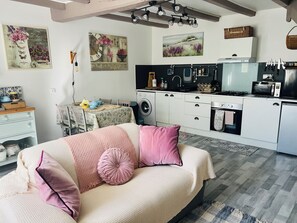 Une chambre confortable avec un lit, des oreillers et une table de chevet. À côté se trouve une petite cuisine équipée d’un évier, d’une cuisinière et d’un four à micro-ondes.
