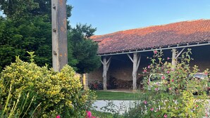 Um jardim com diversas plantas e flores, uma estrutura de pedra e um edifício com telhado em cerâmica.