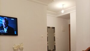 Ett vardagsrum med en platt-TV som är monterad på väggen, en träbänk, en spegel och en liten hylla med blommor.