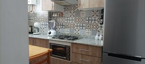 A kitchen with a gas stove, a blender, a coffee maker, and a refrigerator.