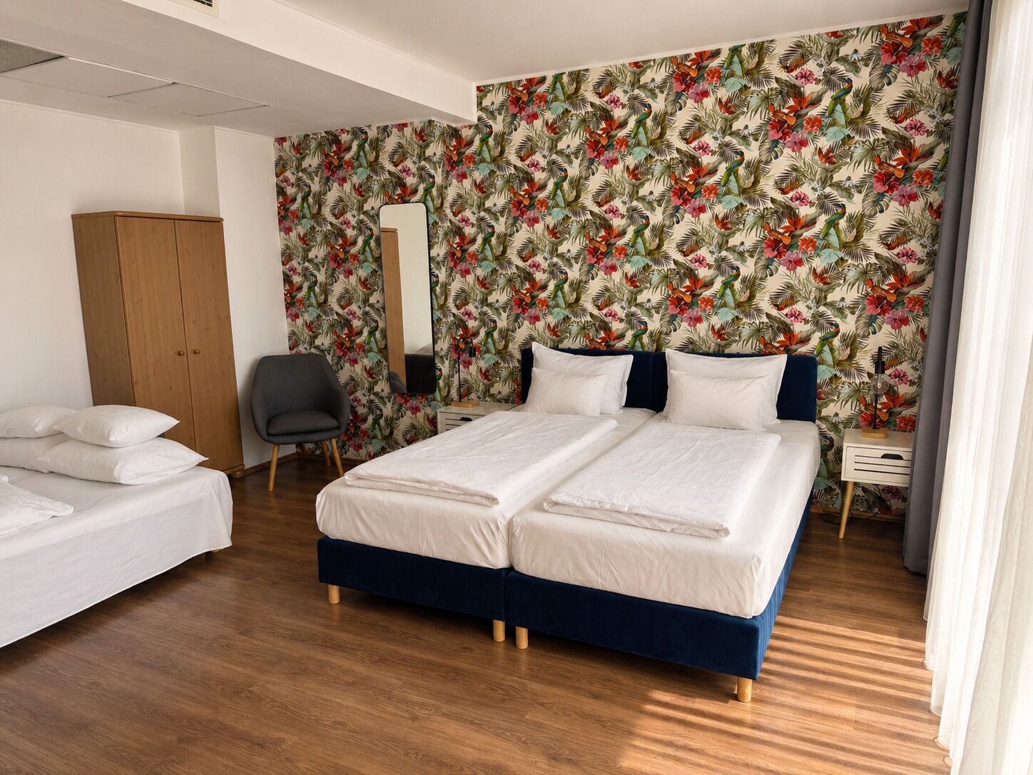 A hotel room with a double bed, a wardrobe, a chair, a bedside table, and a mirror.