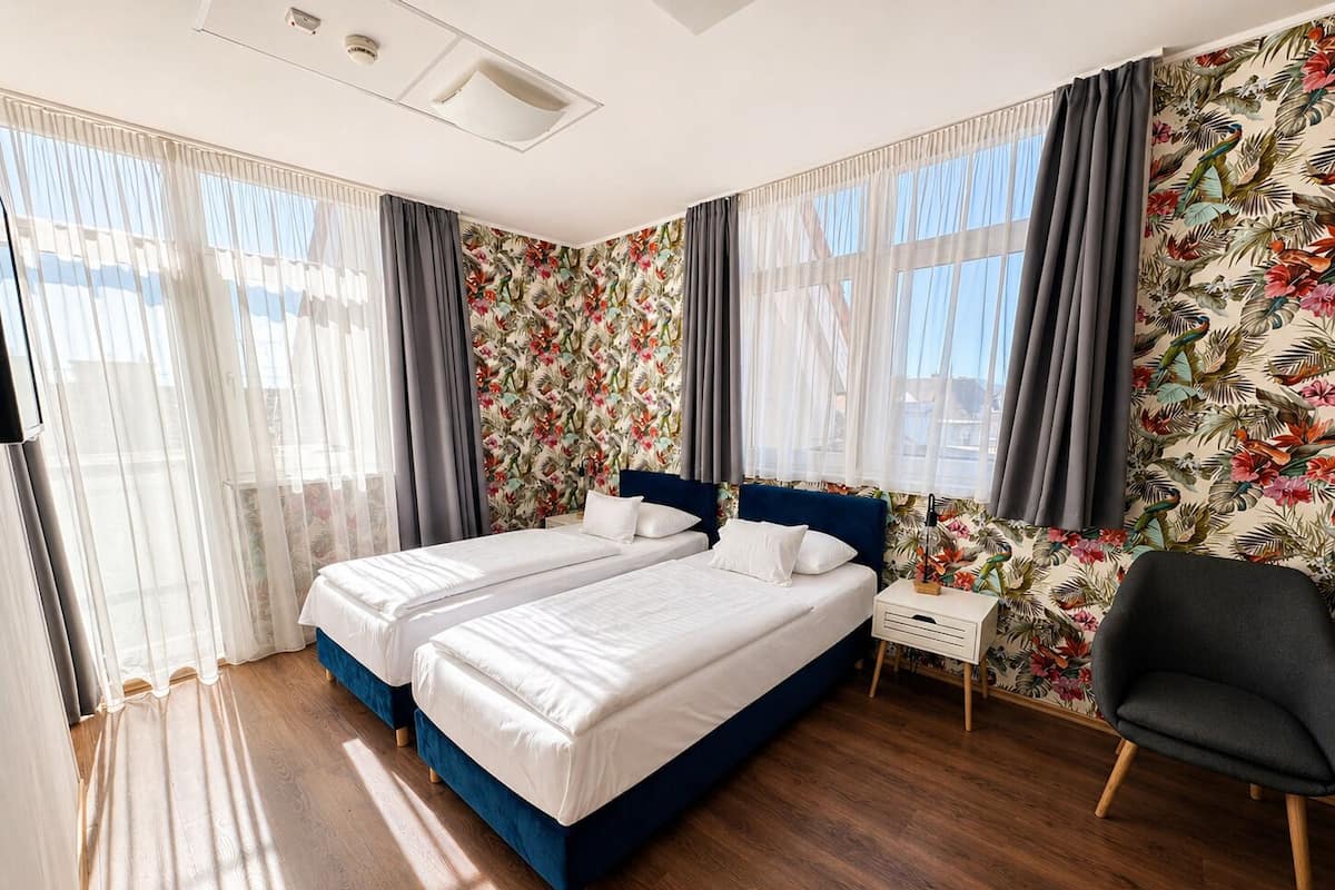 A double bed with a dark headboard, a bedside table, and a chair in a room with wooden flooring and floral wallpaper.