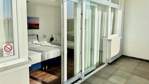 Ein Hotelzimmer mit einem Bett, einem Nachttisch, einem Bild an der Wand und einer Glastür, die auf einen Balkon führt.