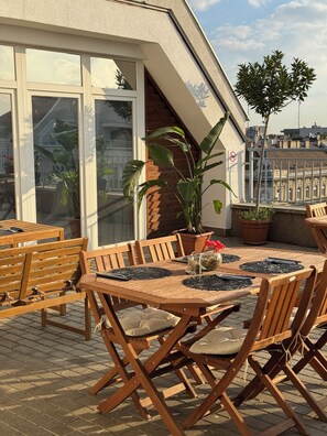 A wooden deck with a table and chairs, potted plants, and a view of the cityscape. - Rooftop City Residence (Budapest)