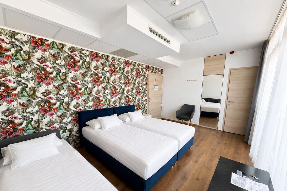 A hotel room with two beds, a desk, a chair, a wardrobe, and a shower area.
