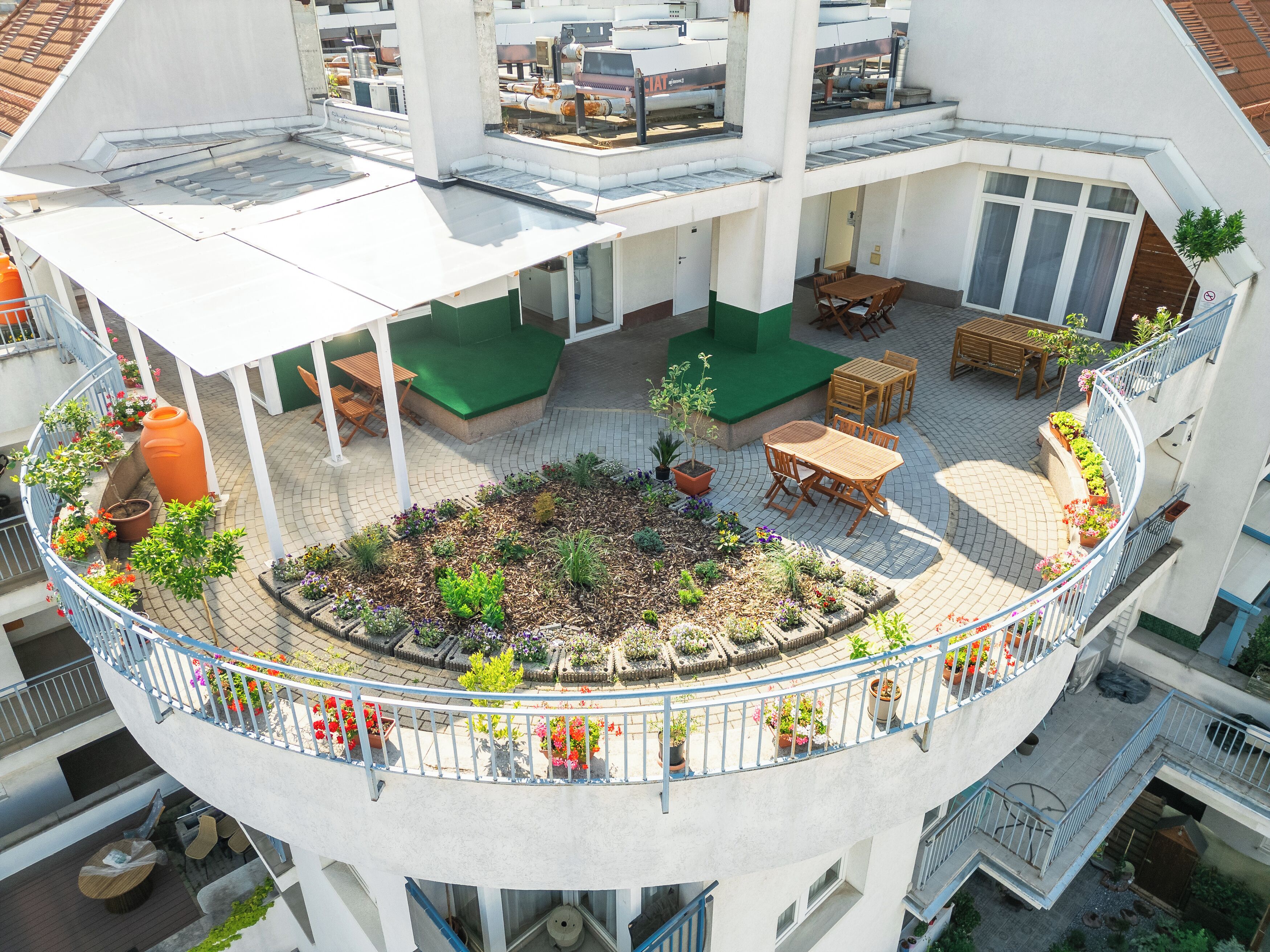 A multi-level outdoor terrace with a central garden, seating areas, and a covered section.