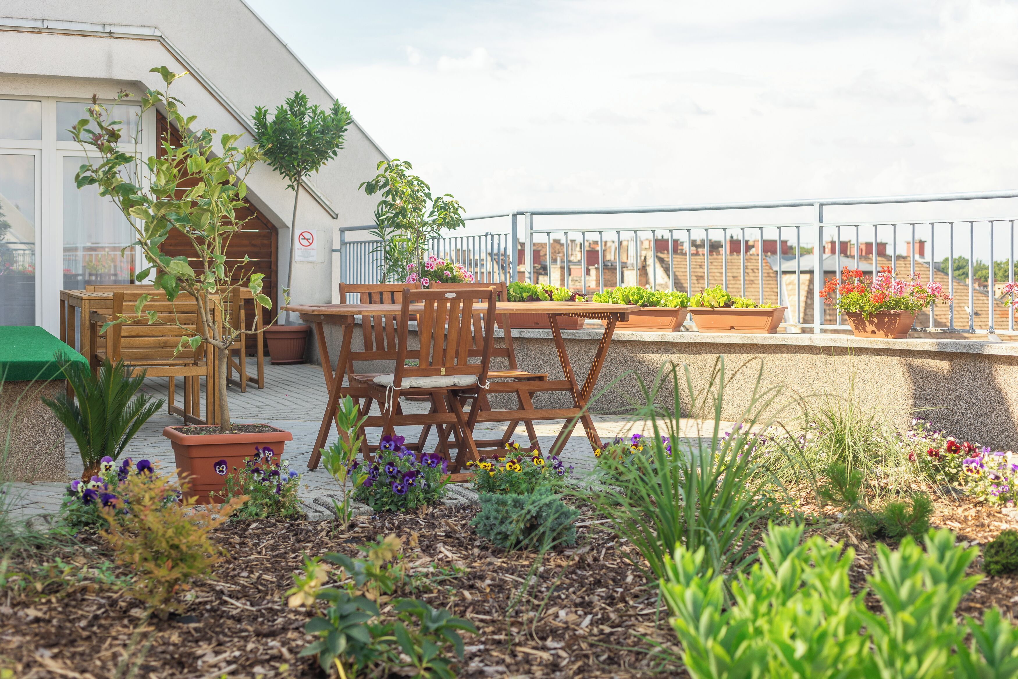 Eine Terrasse mit Holzmöbeln, Blumentöpfen und Blick auf die Stadtlandschaft.