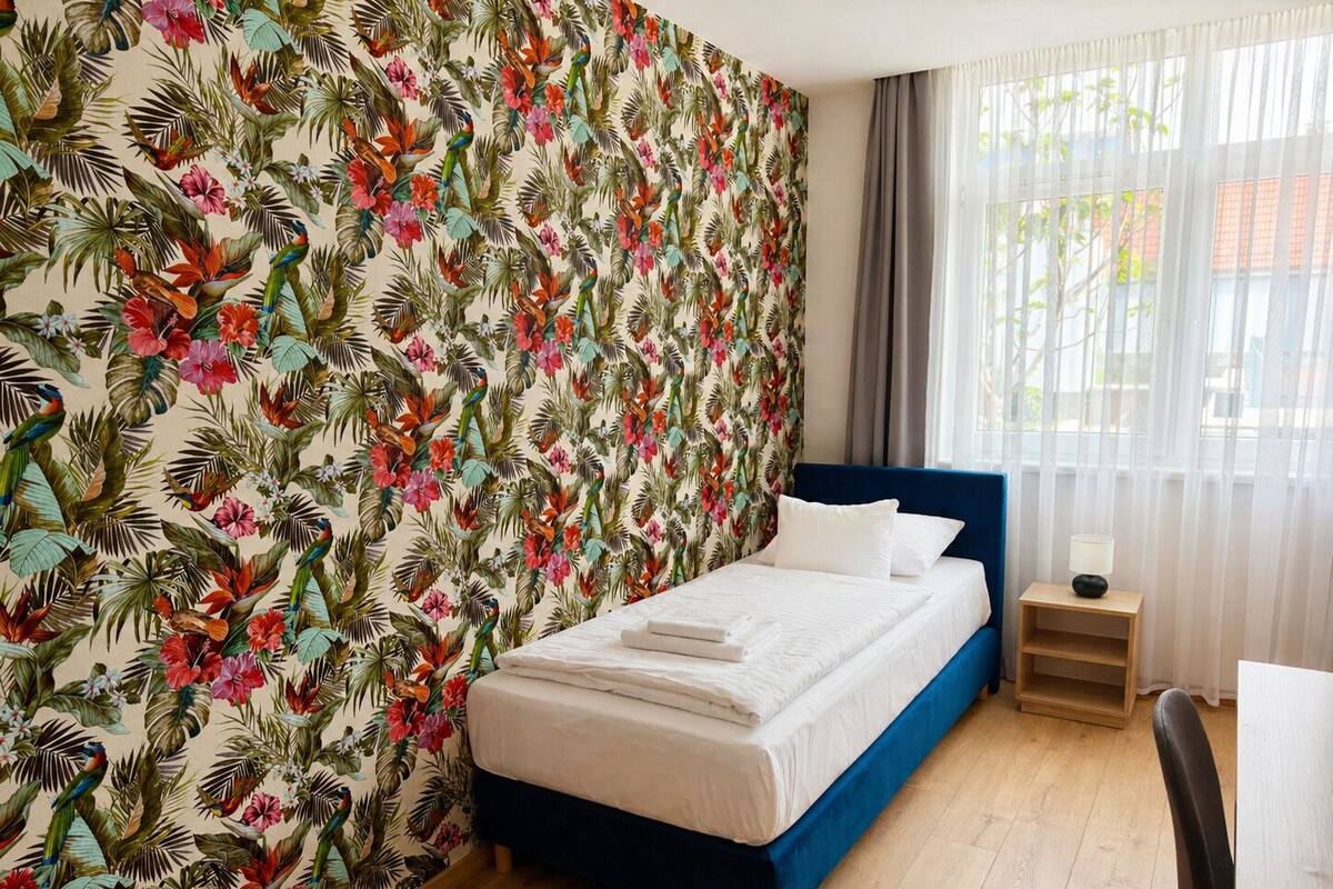 A room with a bed, a nightstand, a chair, and a window with curtains.