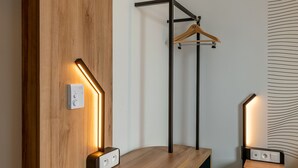 Quarto moderno com parede de destaque em madeira, cabideiro suspenso e duas luminárias fixadas na parede.
