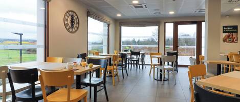 Un vaste espace intérieur doté de nombreuses tables et chaises, de grandes fenêtres donnant sur l’extérieur et d’une horloge au mur.