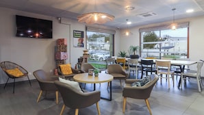 Interior de café moderno, com mesas redondas, assentos confortáveis e grandes janelas com vista para a rua.