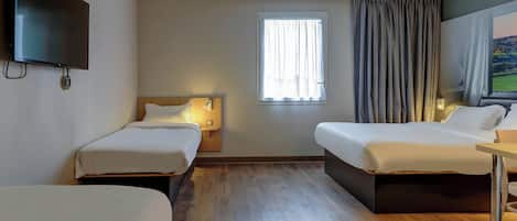 A hotel room with two single beds, a TV mounted on the wall, a window with curtains, and a wooden floor.
