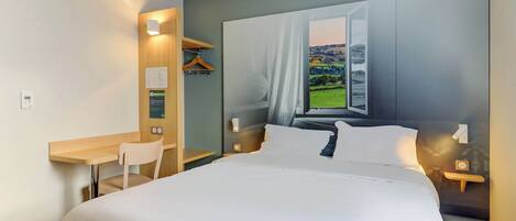 A hotel room with a large bed, a desk, and a chair. There is a window with a view of the countryside.