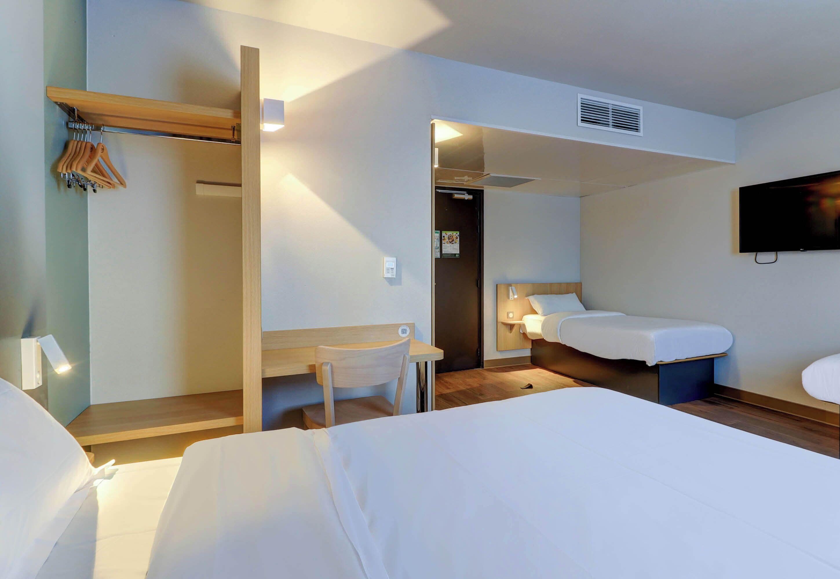 A hotel room with two beds, a desk, a chair, a TV, and a wardrobe.