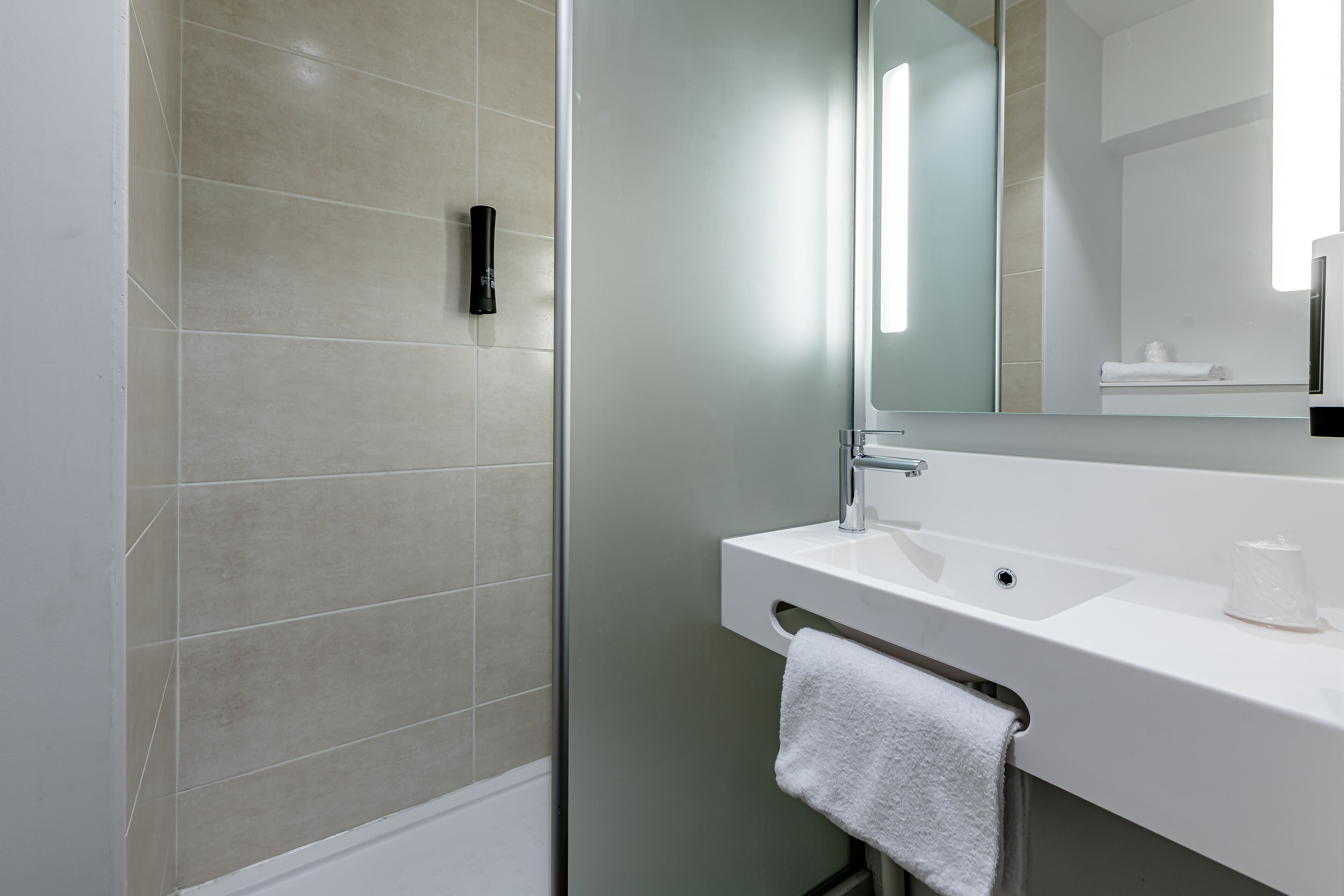 Un baño moderno con cabina de ducha de vidrio, un lavabo blanco y un espejo grande.