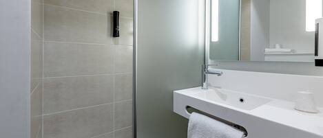 Un baño moderno con cabina de ducha de vidrio, un lavabo blanco y un espejo grande.