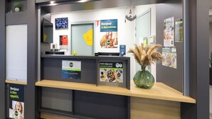 Uma receção com um televisor de ecrã plano, um vaso de planta e diversos cartazes e avisos.