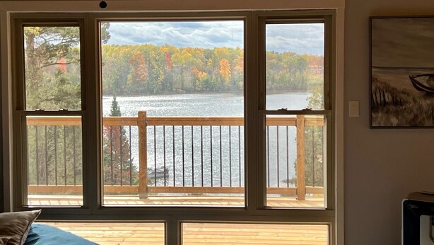 Una habitación con un ventanal grande que da a un lago y follaje otoñal.