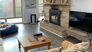 Una sala de estar acogedora con chimenea de piedra, un televisor, una mesa de centro de madera con piezas de ajedrez y un sillón informal azul.