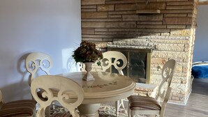 Un comedor con una mesa redonda, seis sillas, un florero decorativo y una chimenea de piedra.