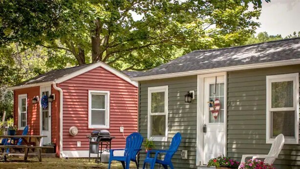 A small, two-story house with a red and gray exterior, a front porch with blue chairs, and a table. - Cabin in the heart of the Hudson Valley, Cabin 4 (Newburgh)