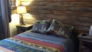 A bedroom with a wooden headboard, a colorful quilt, and a bedside table with a lamp. - Perfect Cabin 5 minutes to Blanchard Springs Nat. Park (Mountain View)