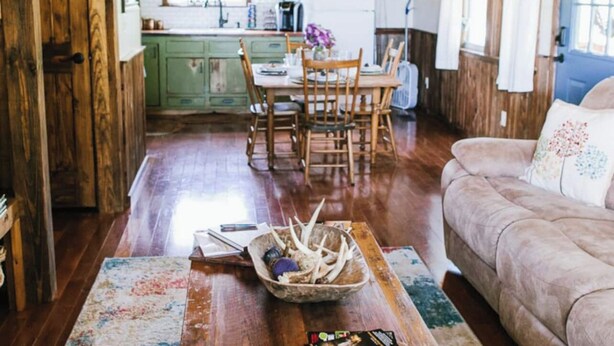 A rustic interior with a wooden ceiling, a dining area with a wooden table and chairs, a sofa, and a kitchen in the background. - Perfect Cabin 5 minutes to Blanchard Springs Nat. Park (Mountain View)
