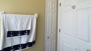 Un baño con una toalla blanca colgada en un perchero, una puerta blanca y un dispensador de papel higiénico en la pared.