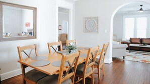 A dining area with a wooden table and chairs, a mirror on the wall, and a view into the living room.