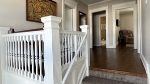 A staircase with white balusters leading to a landing, a framed map on the wall, and a hallway with a door leading to a living room.