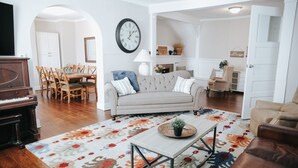 A living room with a sofa, coffee table, and a piano. There is a dining area with chairs and a table.