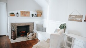 A cozy living room with a fireplace, a comfortable armchair, a white cabinet, and a bench with cushions.