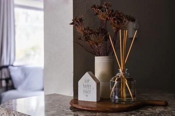A marble countertop with a small house-shaped sign reading "our happy place," a glass vase with dried flowers, and a wooden spoon. - McCall Suite Spot: 1-bedroom with indoor fireplace (McCall)