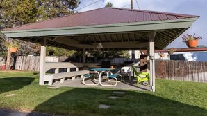 Un'area picnic riparata con tavolo e panche, circondata da una recinzione in legno e alberi.
