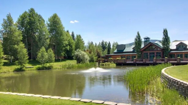 Uma pousada com um lago, rodeada por árvores e um gramado bem cuidado.
