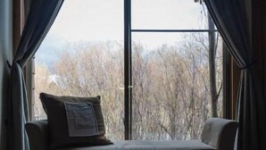 Quarto com uma janela grande, um sofá com almofada e vista para árvores.