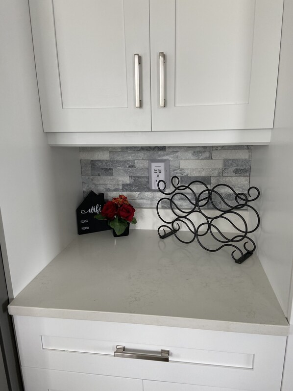 A kitchen with white cabinets, a grey countertop, a black metal rack, and a small vase with red flowers. - Book Away. Gulf Home-Pool, dock,ramp,Fish Gear,kayaks,paddle boards, Elevator (Hudson)
