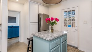 A modern kitchen with a granite countertop, a stainless steel refrigerator, and a vase with pink roses. - The Downtown Velvet Adobe (Santa Fe)