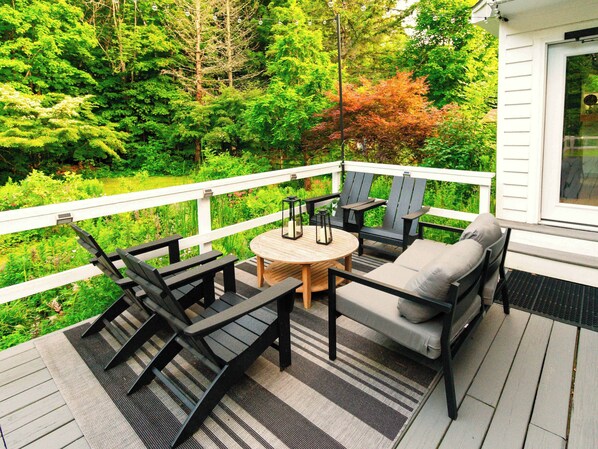 A deck with outdoor furniture, a round table, and a view of a lush garden. - Artist Bluff — Signature King Suite with Living Room & Fireplace (Lincoln)