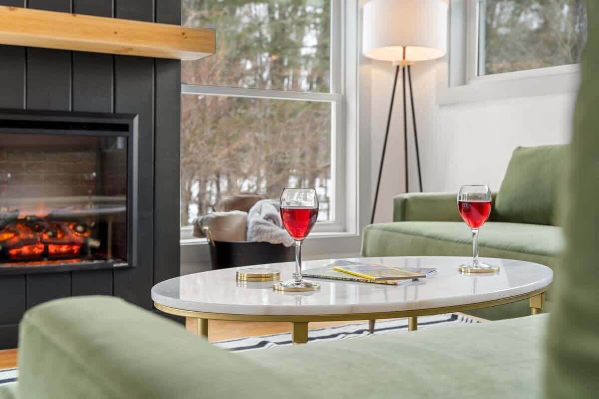 A cozy living room with a fireplace, a round coffee table with two glasses of red wine, and a green sofa.