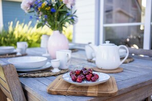 Een houten tafel met een schaal kersen, een witte theepot en een bloevas.